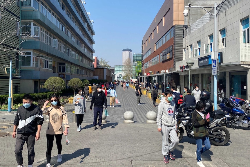 A photo of lots of people walking through an outdoor shopping plaza