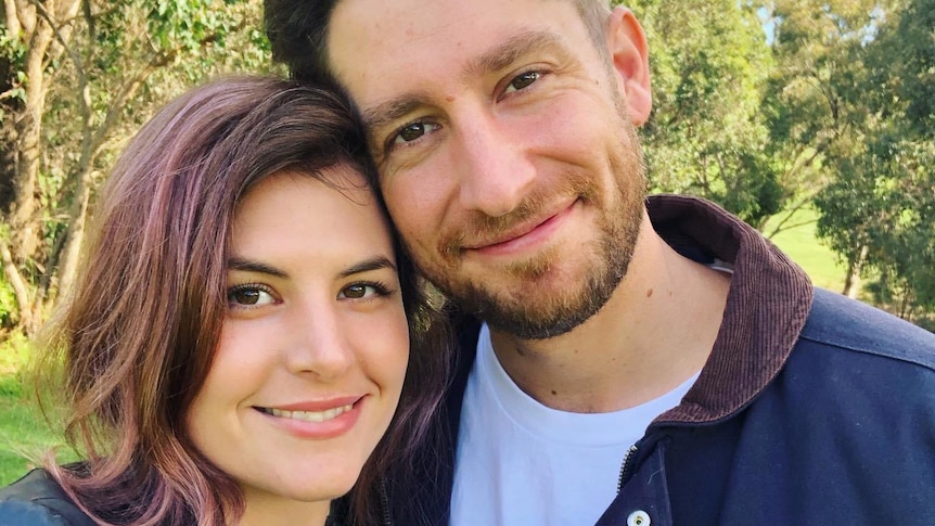 A head and shoulders shot of a young smiling couple posing for a photo outdoors.