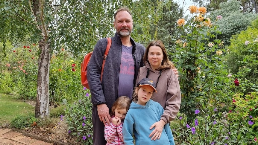 A picture of four people, standing in front of plants on a path, two adults a man and a woman and two children.