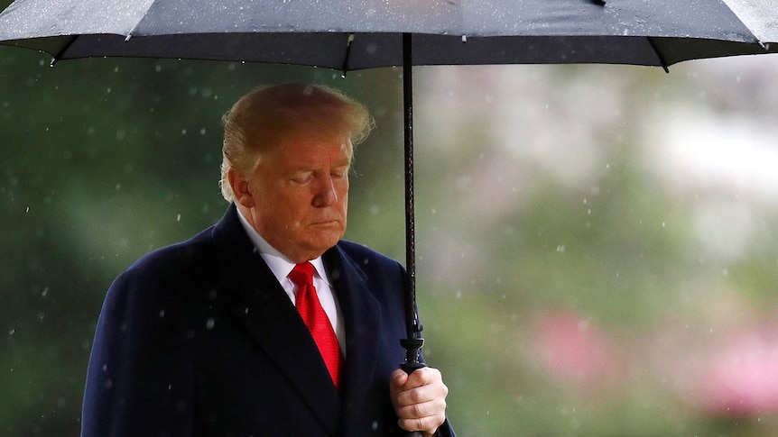 Donald Trump holds an umbrella in the rain