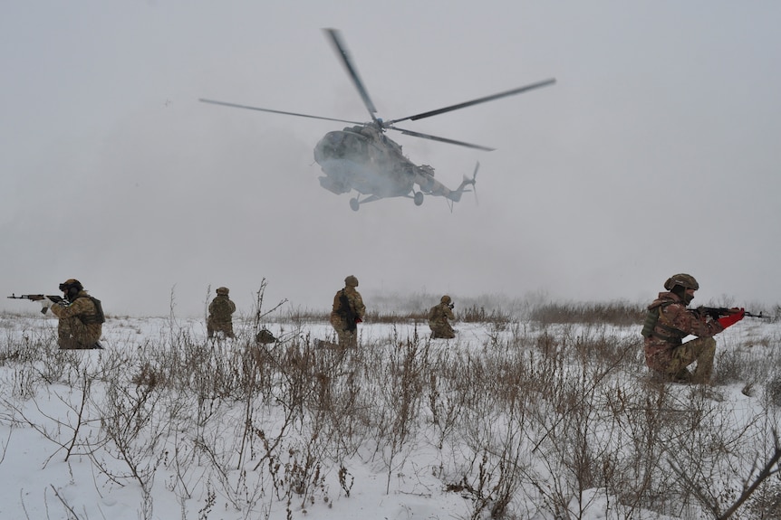 Uzbrojeni żołnierze na śniegu, a helikopter unosi się tuż nad nim.