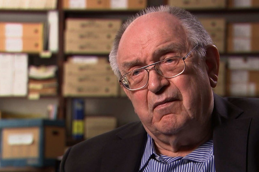 German microbiologist and Stasi files researcher Dr Werner Franke sits in front of rows of files.