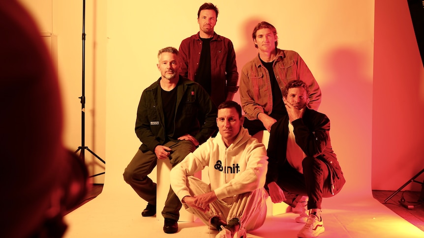 Five men pose against a white backdrop screen for a photoshoot