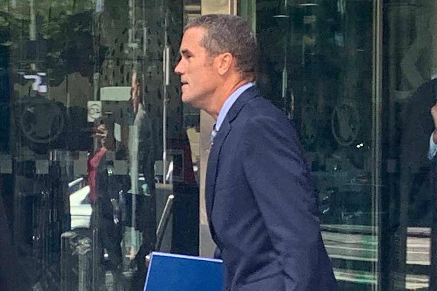 Ross Fowler, with short slightly greying hair, walks out of a courthouse wearing a blue suit and blue shirt.