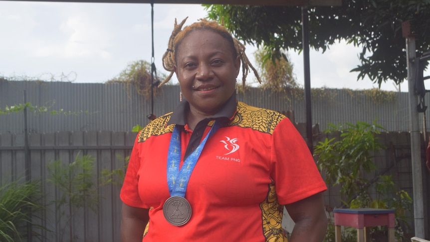 A Papua New Guinean woman wearing a red shirt and a medal around her neck smiles at the camera. 