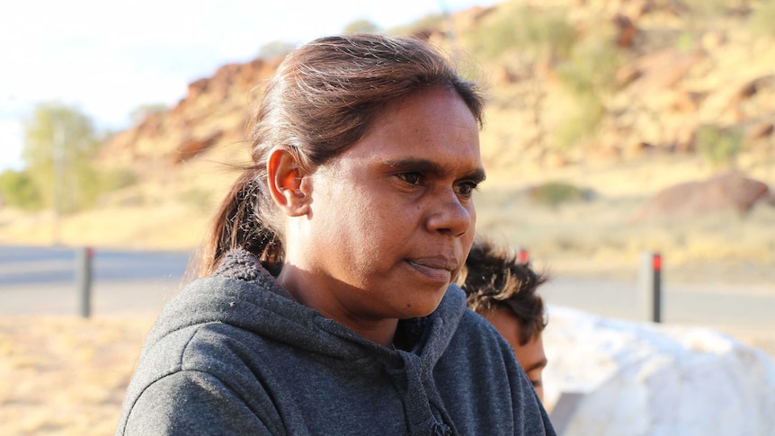 Shirleen Campbell wearing a grey jumper with central australian bush out of focus in the distance.