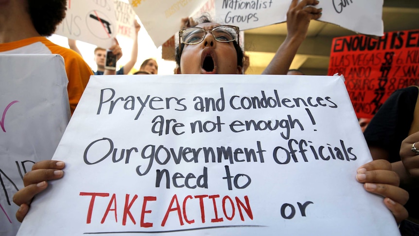 A protester holds  sign reading "prayers and condolences are not enough