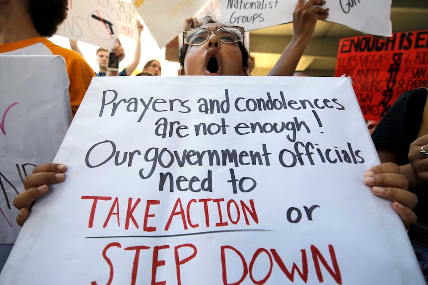 A protester holds  sign reading "prayers and condolences are not enough