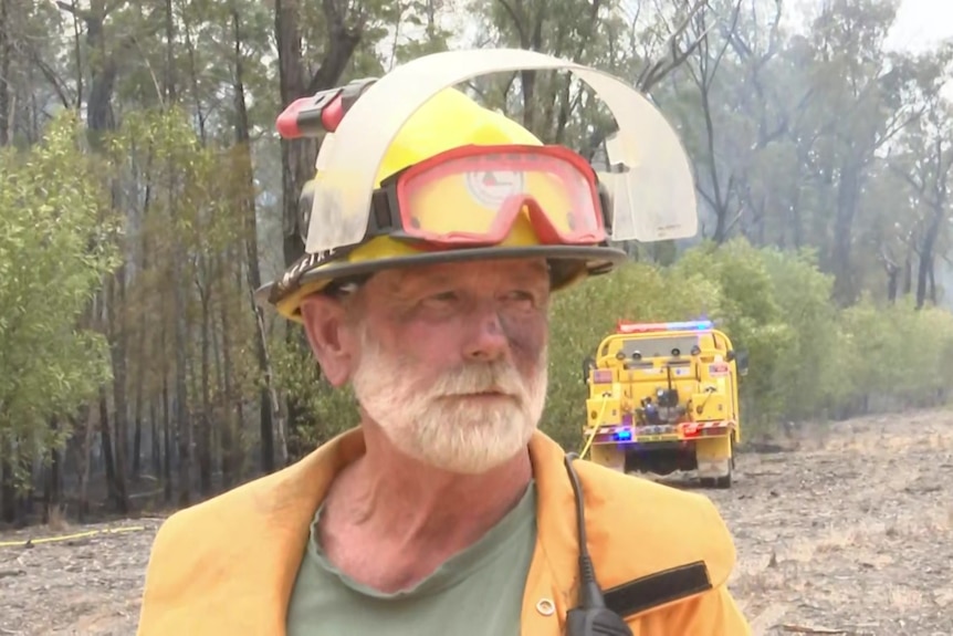 Trevor Watson wears PPE and stands in front of a fire truck