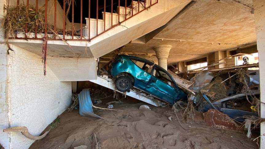 A wrecked car up a staircase with flood debris everywhere around it