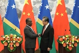 In front of a row of Solomon Islands and Chinese flags, Jeremiah Manele and Wang Yi shake hands in between lecterns.