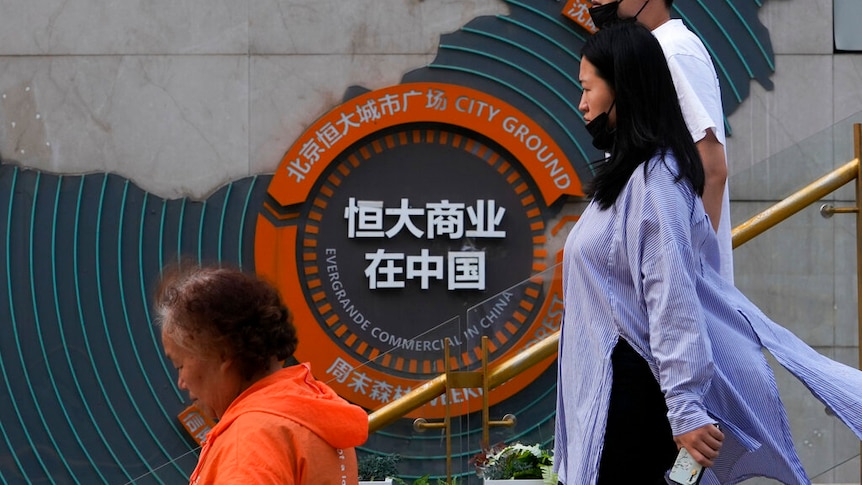 People walk by an orange logo for Evergrande.