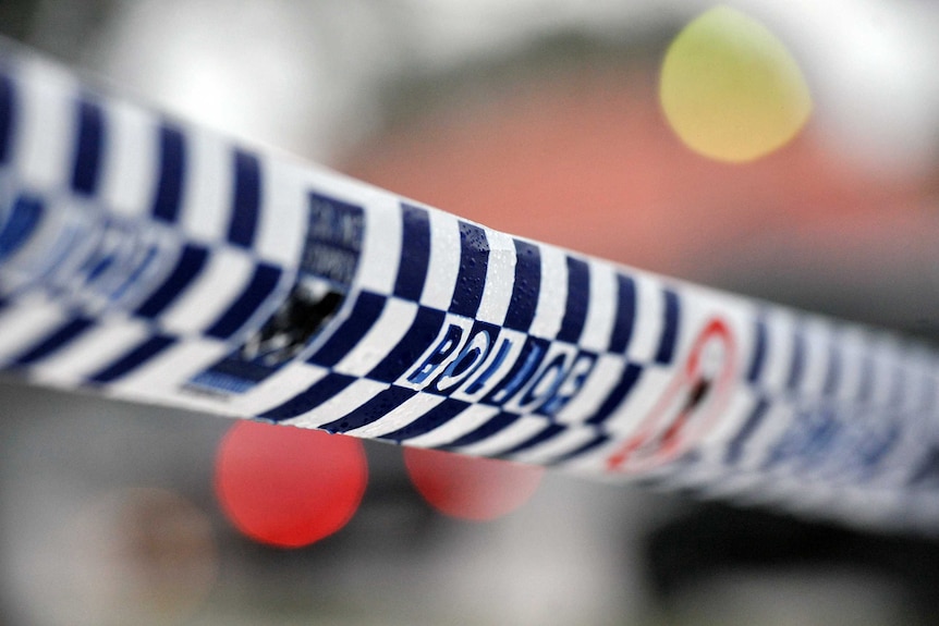 Generic image of police tape strung up across an out of focus crime scene.