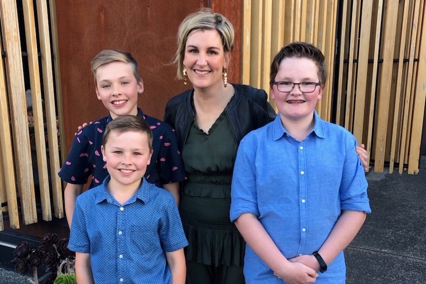 A woman with three young boys, all smiling at the camera