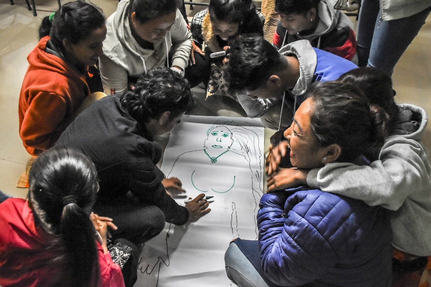 People sit around a drawing of a woman's body at the Sounali crossing on the Nepal-India border.