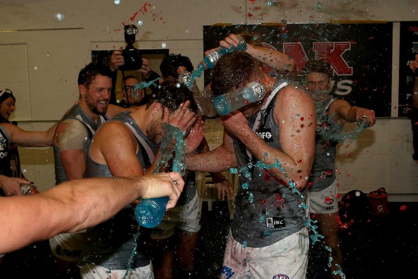AFL players celebrate their first win in the rooms after the game.