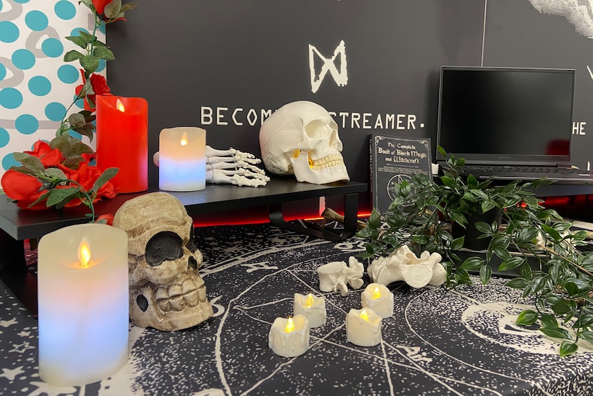 Table with candles, fake skulls, fake plants and a laptop.