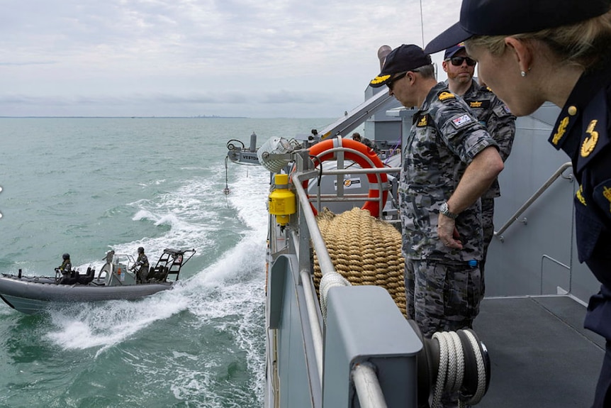 Border force officers in uniforms watch smaller patrol boat depart ship
