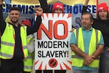 Workers stand with a sign that says 'no modern slavery'.