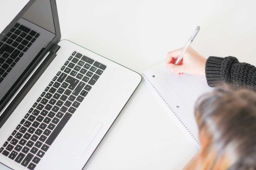 Close up of woman writing in a notebook and an open laptop representing financial research that can help you get out of debt.