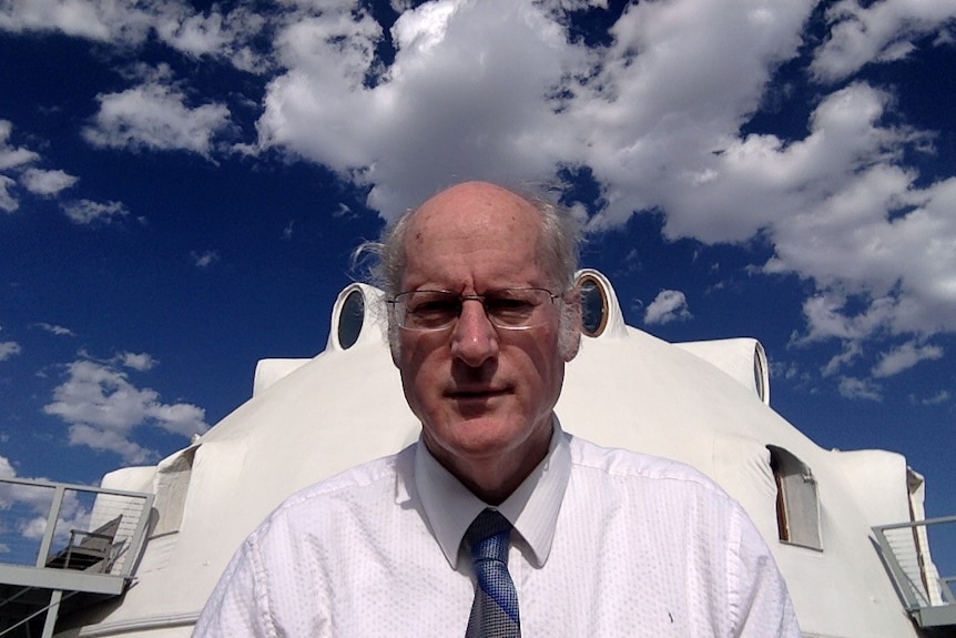 Older man in business shirt and glasses stands in front of dome home