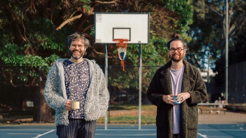 two men stand in a basketball court holding a cup of tea each
