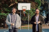 two men stand in a basketball court holding a cup of tea each