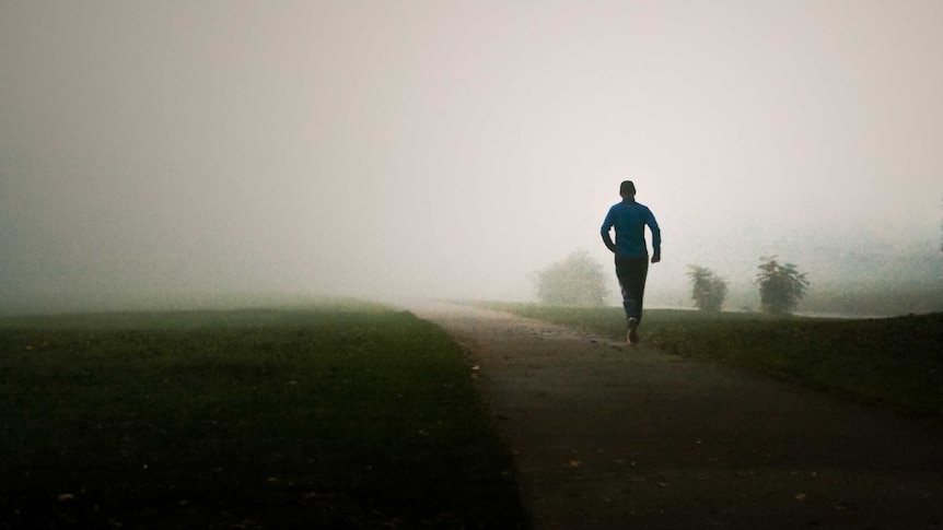 Rear view of a man running along a country track in the fog