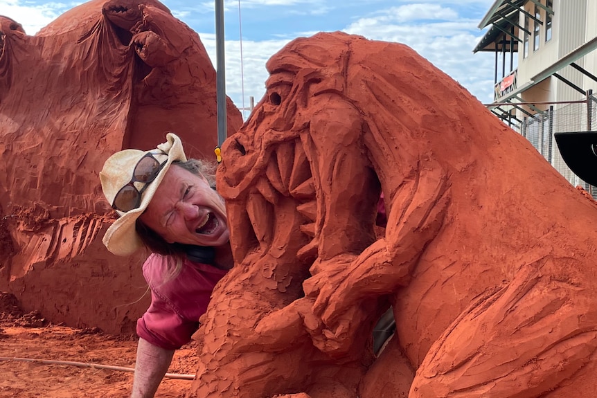 a man and a woman, both wearing hats, muck around in front of dinosaur sculpture 