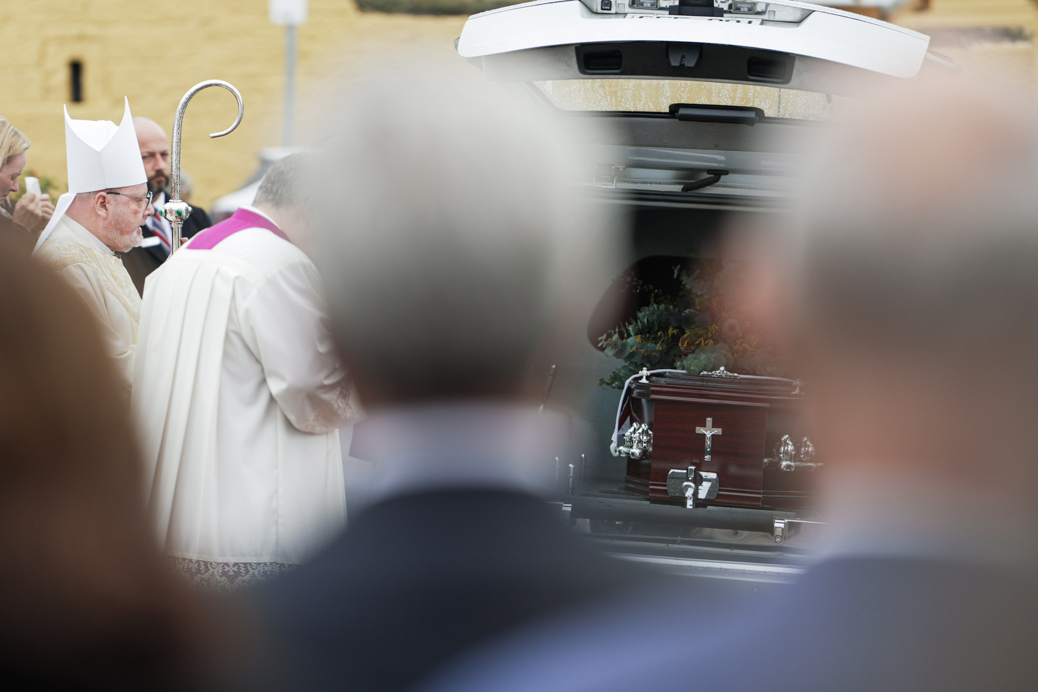 Archbishop Tony Ireland stands at the back of a hearse which holds Michael Tate's coffin.