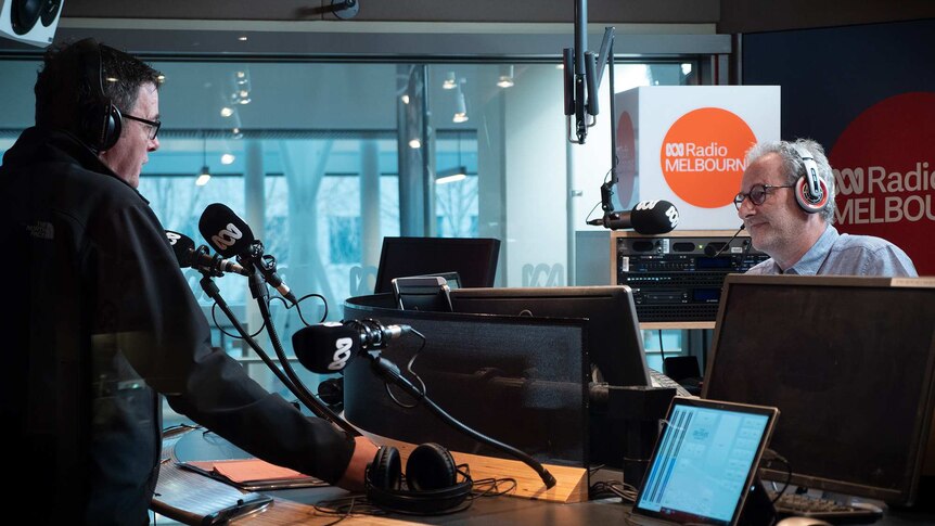 Daniel Andrews and Jon Faine face each other over a desk inside a radio studio.