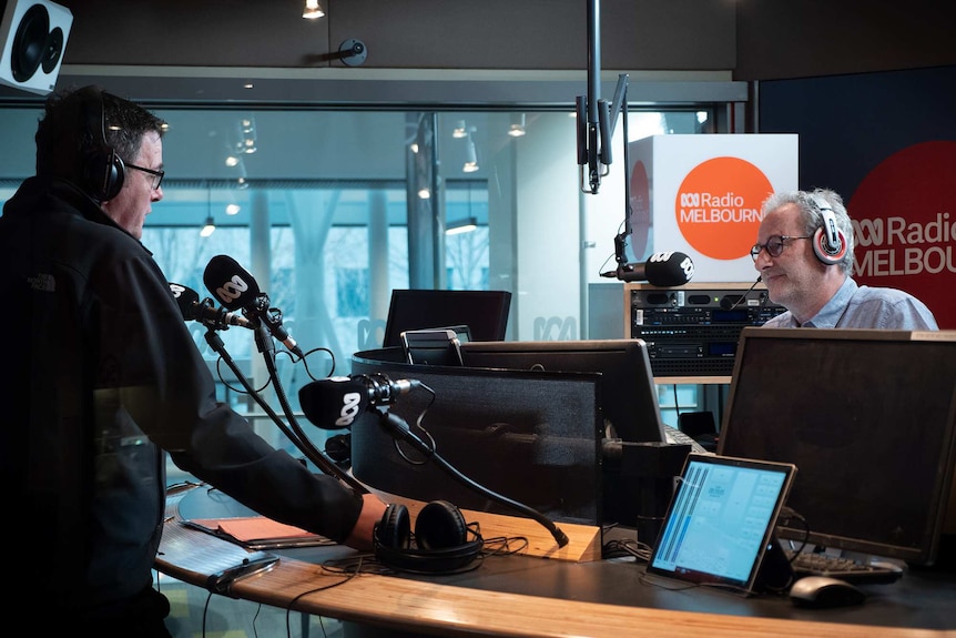 Daniel Andrews and Jon Faine face each other over a desk inside a radio studio.