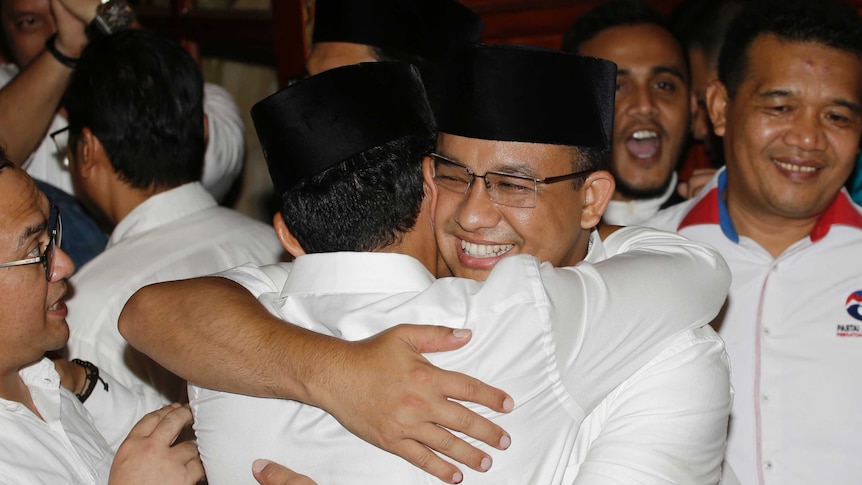 Gubernatorial candidate Anies Baswedan hugs his running mate Sandiaga Uno in a crowd of people dressed in white.