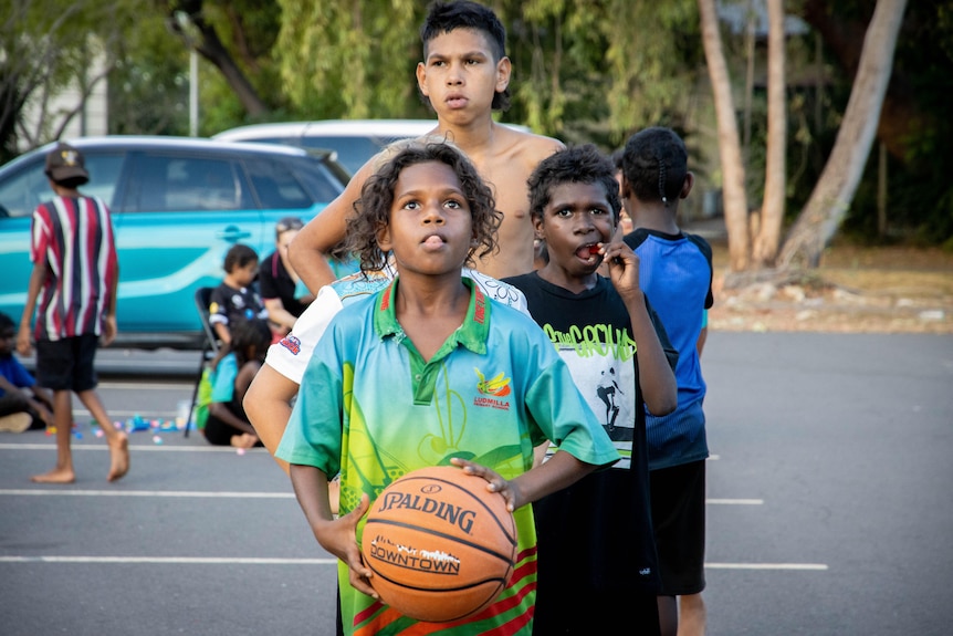 A young Indigenous boy about to shoot a basketball towards a hoop, with other boys lined up behind him