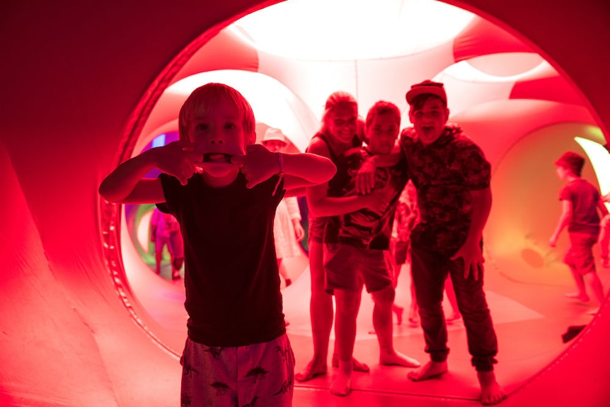 Children pulling faces under red lights in the Arboria luminarium at Womadelaide.