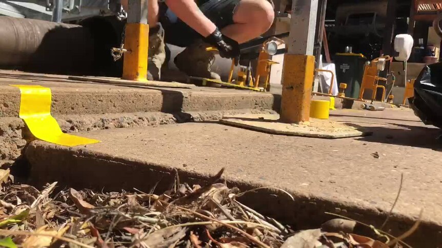 A tradesman squats on a concrete slab between two braces.