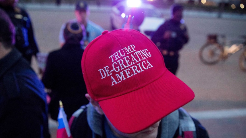 A man wears a red hat that reads Trump de-greating america