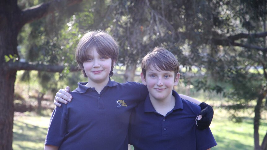 Two boys aged about 11-years-old standing arm in arm smiling at the camera.