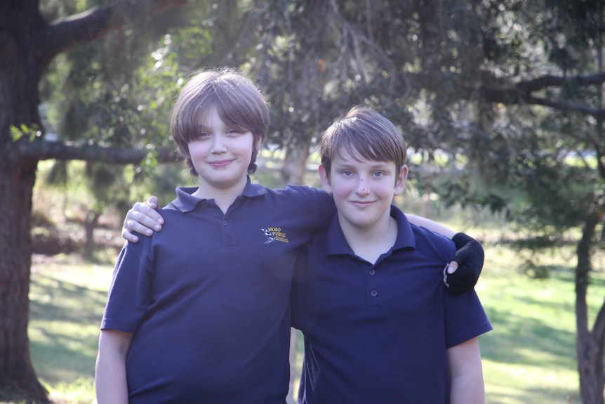 Two boys aged about 11-years-old standing arm in arm smiling at the camera.