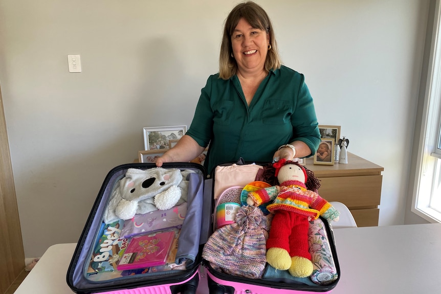 Woman standing behind an open suitcase containing toys, clothes and books. 