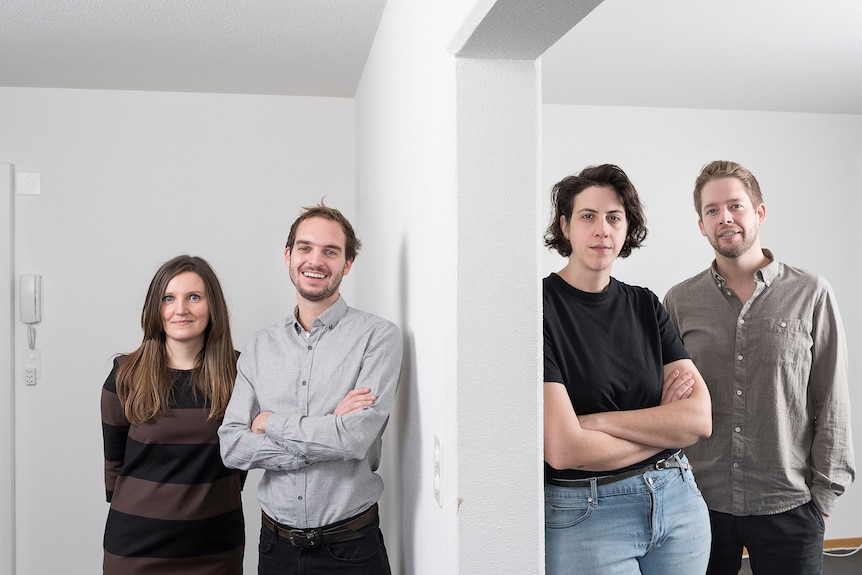 Four young architects standing in a white space, separated by a wall