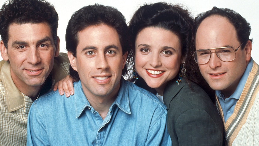 Colour photo of Kramer, Jerry, Elaine and George huddled close together, smiling.