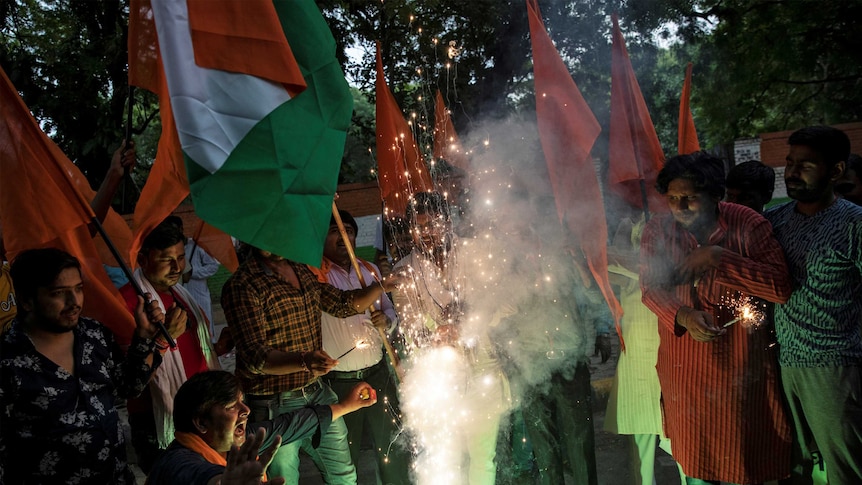 A group of Indian men holding Indian flags light fireworks