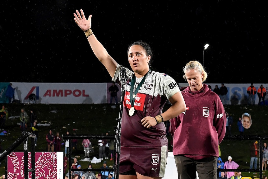 Tazmin Gray stands on stage with a medal around her neck and waves to the crowd.