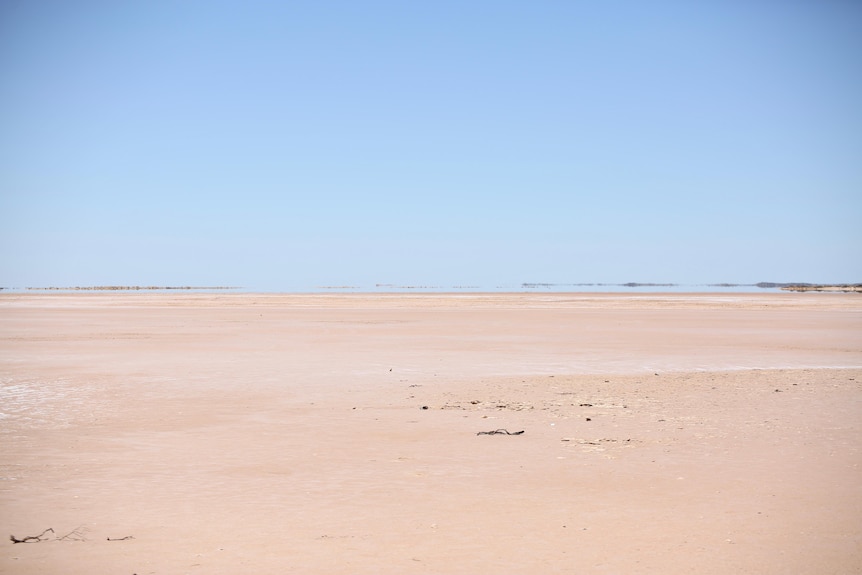 A wide shot of a sand plain underneath a pale blue sky.