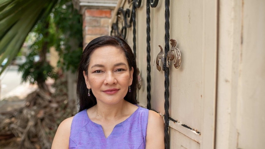 A smiling, neat-looking woman in a purple shirt in front of a fancy gate