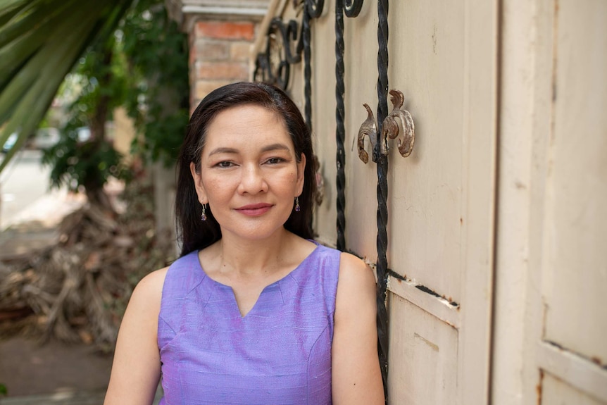 A smiling, neat-looking woman in a purple shirt in front of a fancy gate