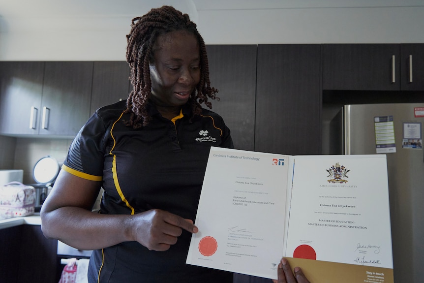 a woman stands in a kitchen looking at several tertiary graduation documents