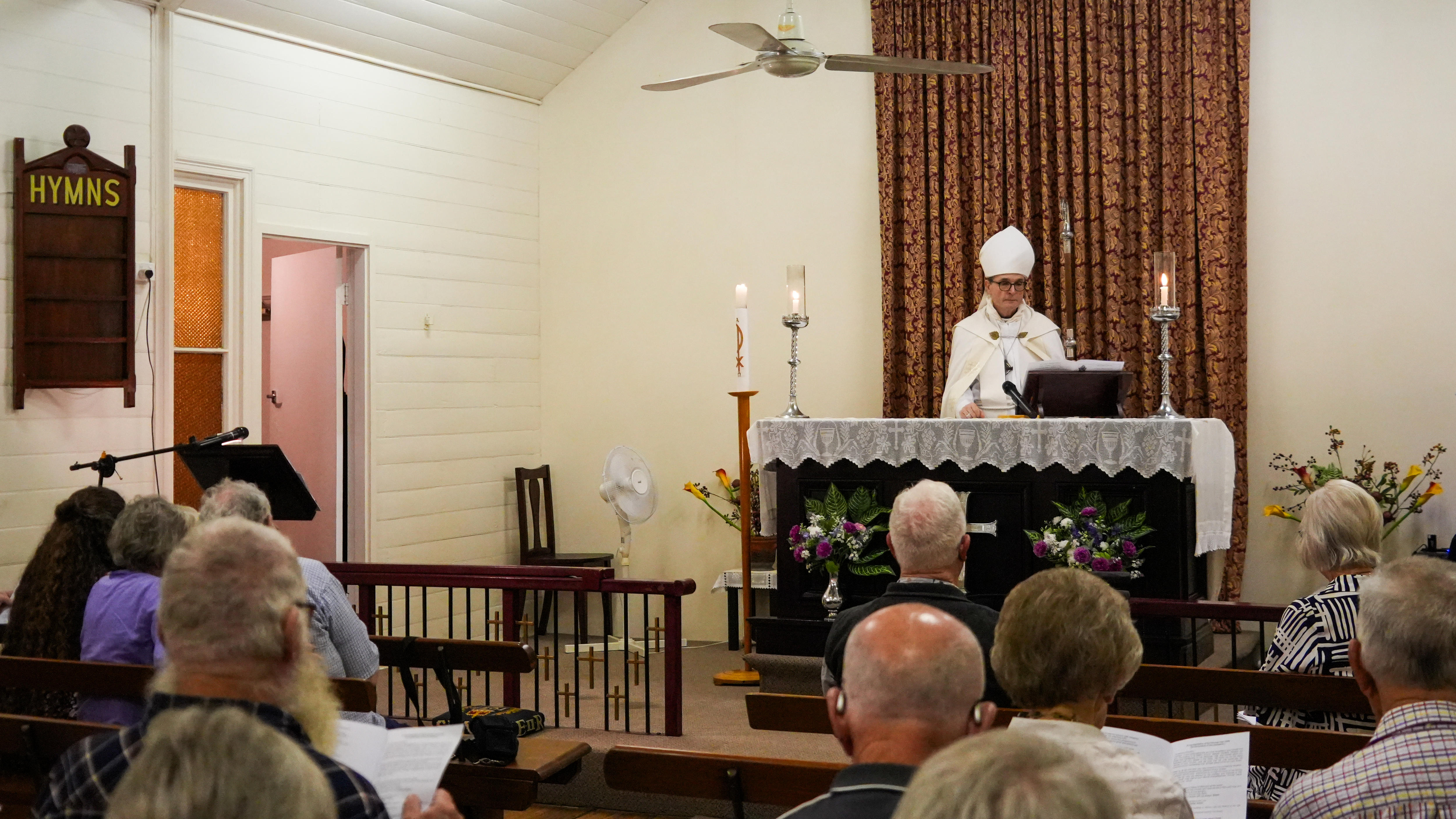 A bishop stands in front of an altar, speaking to congregants