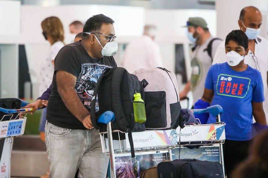 A man wearing a mask and a black shirt pushes a trolley with backpacks on it.